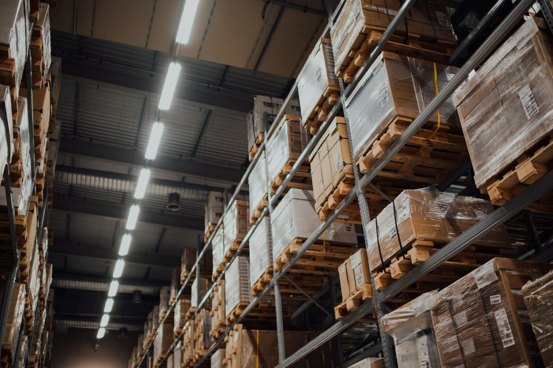 Warehouse aisle with tall pallet racking holding stacked cartons and shrink-wrapped pallets